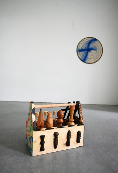 Wooden kit on the floor and circular feathered art piece on the wall