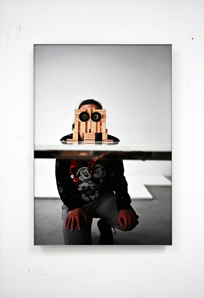 Photograph of a crouching girl behind a wooden sculpture